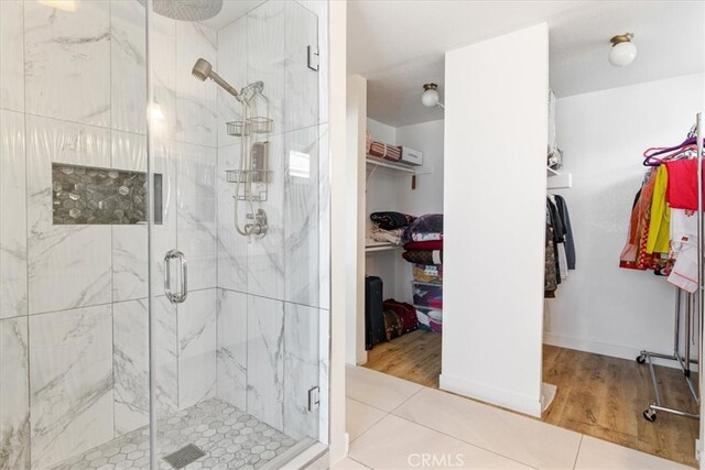 full bath featuring a walk in closet, a marble finish shower, and wood finished floors