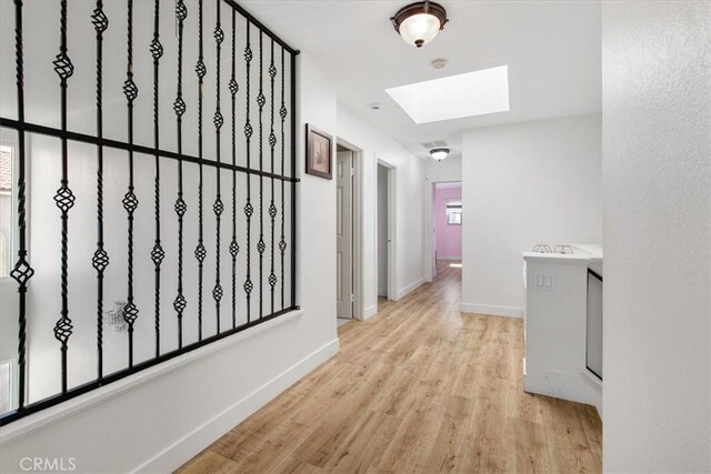 hallway featuring baseboards, a skylight, and wood finished floors