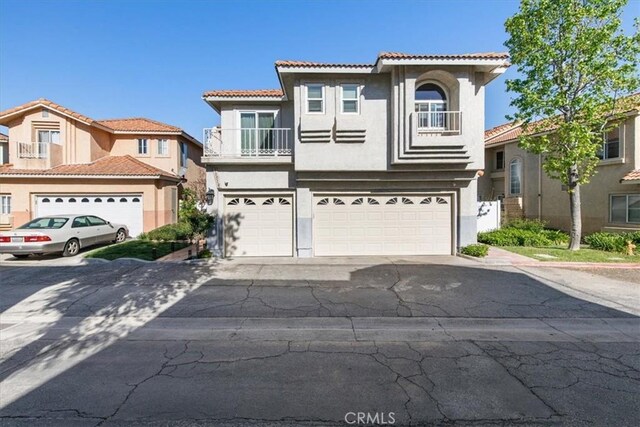 view of front facade featuring driveway, a tile roof, a garage, a balcony, and stucco siding