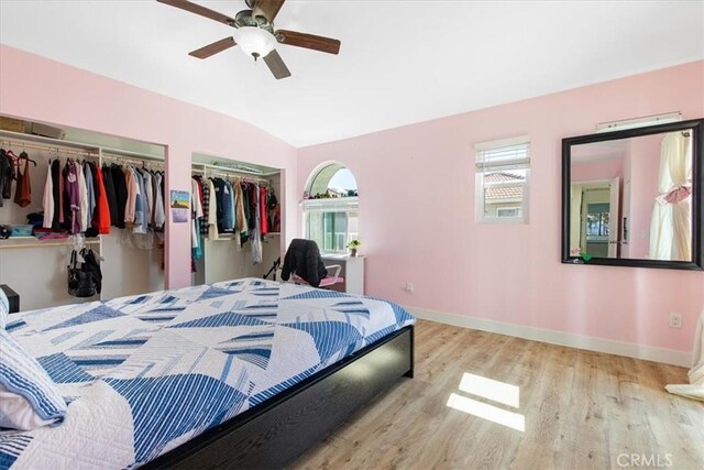 bedroom with vaulted ceiling, baseboards, two closets, and wood finished floors