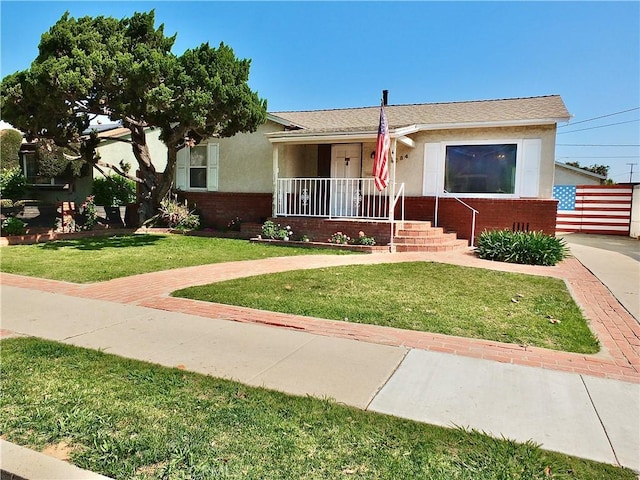 view of front of house with brick siding, a front lawn, stucco siding, and covered porch