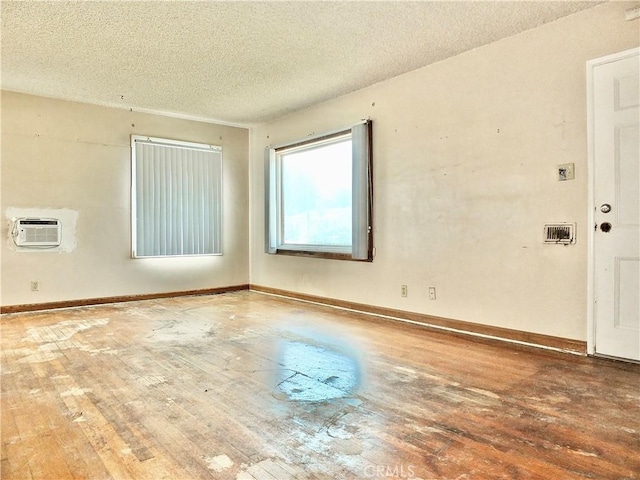 empty room with baseboards, wood-type flooring, a textured ceiling, and a wall unit AC