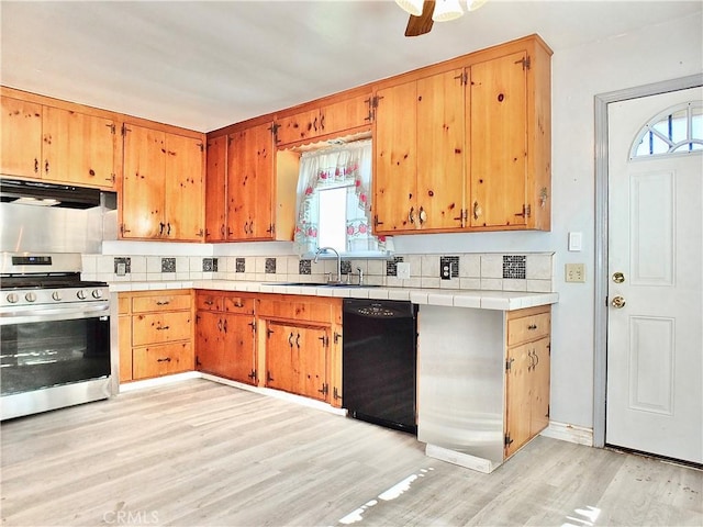 kitchen featuring a sink, gas stove, light wood-style flooring, black dishwasher, and under cabinet range hood