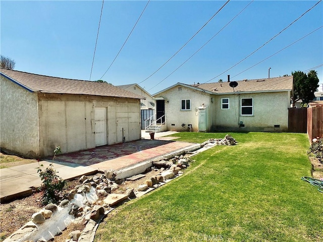 rear view of property featuring fence, an outbuilding, stucco siding, and a lawn