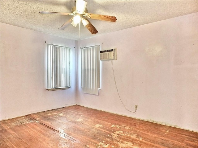 empty room featuring a textured ceiling, a wall mounted air conditioner, a ceiling fan, and wood finished floors