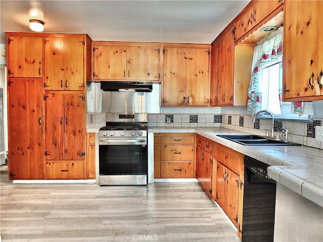 kitchen with black dishwasher, stainless steel gas range oven, tile counters, under cabinet range hood, and a sink