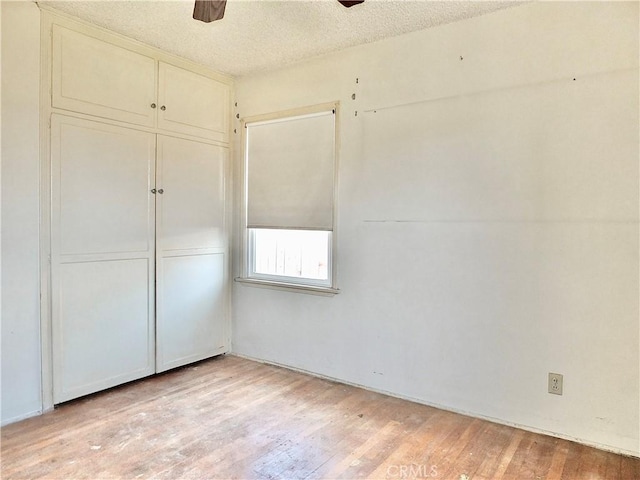 unfurnished bedroom with light wood-type flooring, a textured ceiling, ceiling fan, and a closet