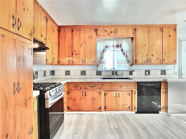 kitchen with a sink, gas stove, black dishwasher, light wood-type flooring, and under cabinet range hood