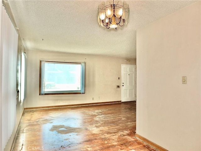 unfurnished room featuring baseboards, a textured ceiling, an inviting chandelier, and wood finished floors