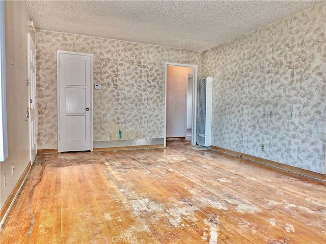 spare room with a heating unit, a textured ceiling, hardwood / wood-style flooring, and wallpapered walls