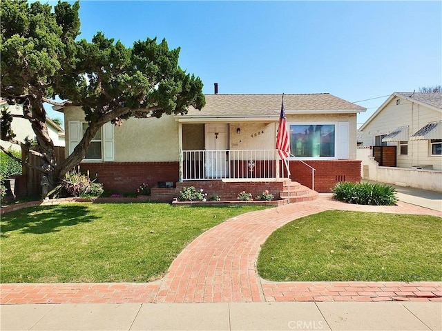 view of front of property with covered porch, brick siding, a front yard, and stucco siding