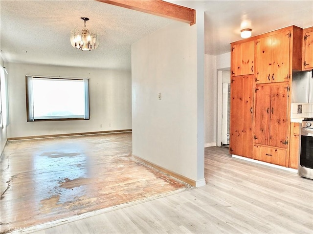 empty room featuring an inviting chandelier, a textured ceiling, light wood finished floors, and baseboards