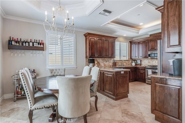kitchen with a raised ceiling, ornamental molding, stainless steel appliances, and visible vents