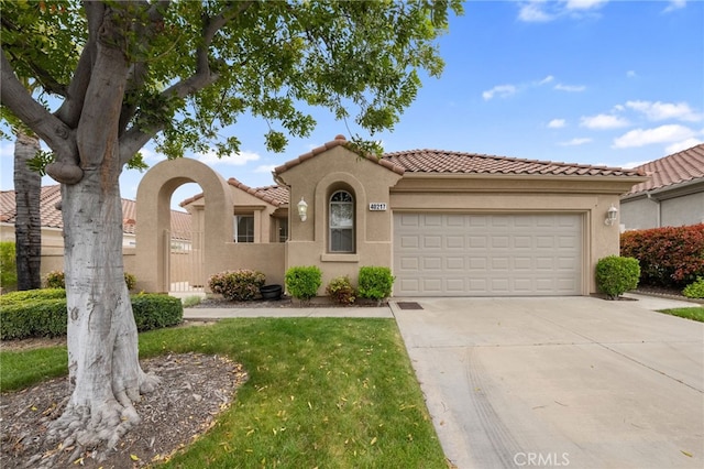 mediterranean / spanish house featuring concrete driveway, stucco siding, a tile roof, and a garage