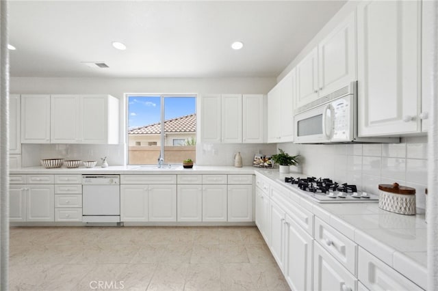 kitchen with white cabinets, a sink, white appliances, backsplash, and visible vents