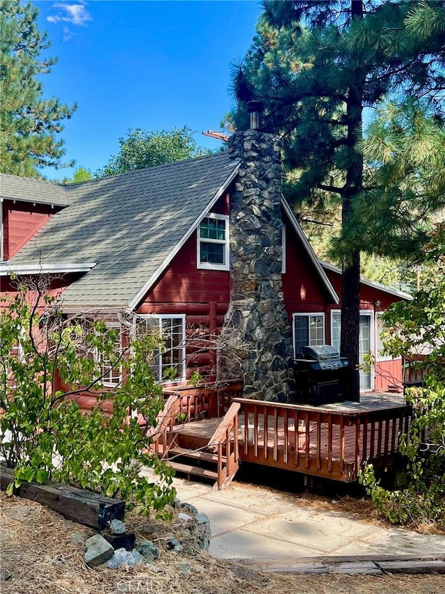 view of front of house with a deck, a chimney, and roof with shingles