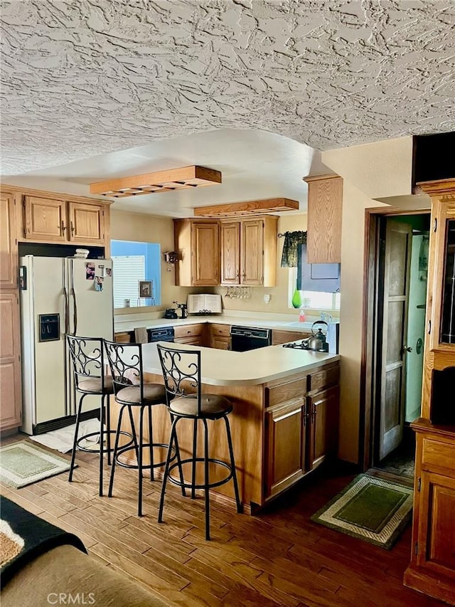 kitchen featuring a peninsula, wood finished floors, black dishwasher, light countertops, and white fridge with ice dispenser