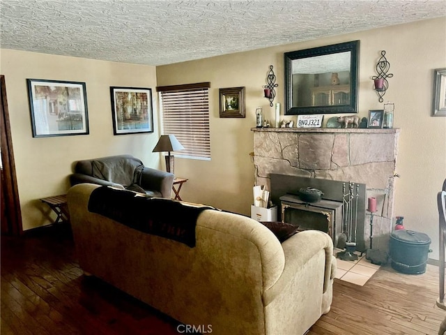 living room with wood-type flooring, a textured ceiling, and a stone fireplace