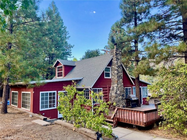exterior space featuring a chimney, a shingled roof, and a deck