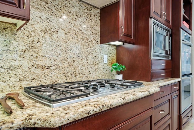 kitchen featuring light stone countertops, appliances with stainless steel finishes, decorative backsplash, and reddish brown cabinets