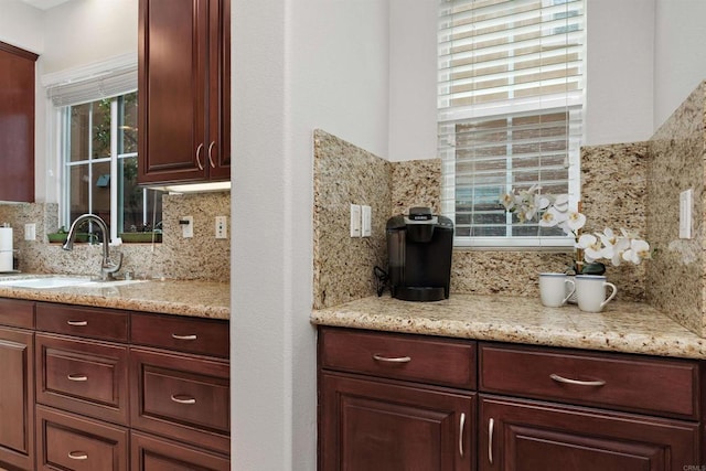 kitchen featuring dark brown cabinets, light stone countertops, decorative backsplash, and a sink