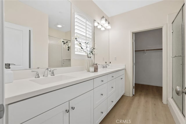 full bathroom with double vanity, a sink, wood finished floors, and a shower stall