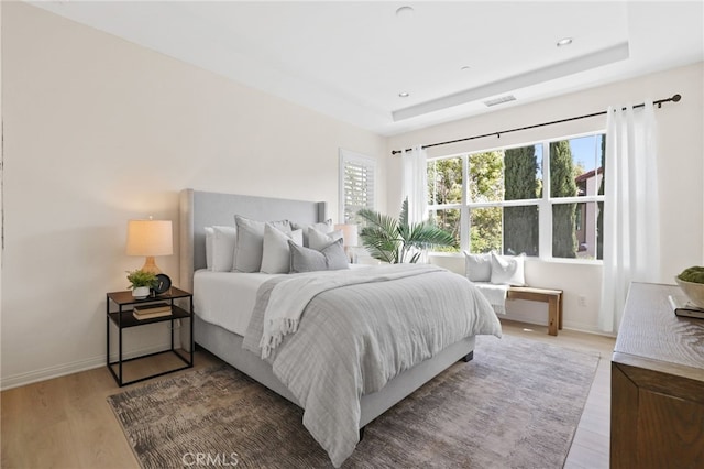 bedroom with baseboards, a tray ceiling, and light wood finished floors