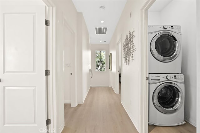 laundry room with laundry area, stacked washer / dryer, visible vents, light wood-type flooring, and baseboards