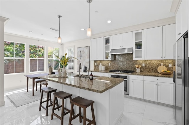 kitchen featuring marble finish floor, under cabinet range hood, a sink, dark stone countertops, and stainless steel appliances