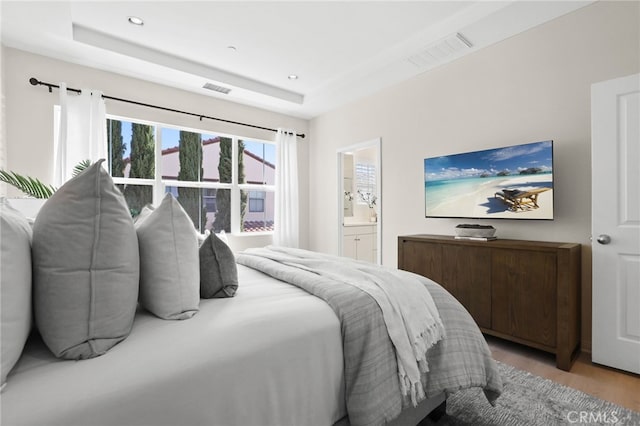 bedroom with light wood-type flooring, a raised ceiling, and visible vents