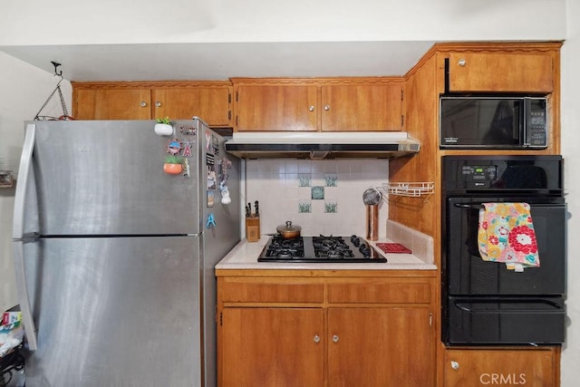 kitchen with under cabinet range hood, brown cabinets, black appliances, and tasteful backsplash