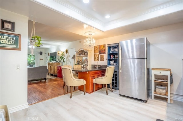 kitchen with crown molding, an inviting chandelier, light wood finished floors, a breakfast bar area, and freestanding refrigerator