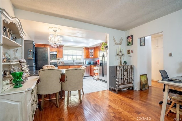 kitchen featuring brown cabinets, a sink, a notable chandelier, light wood-style floors, and stainless steel appliances