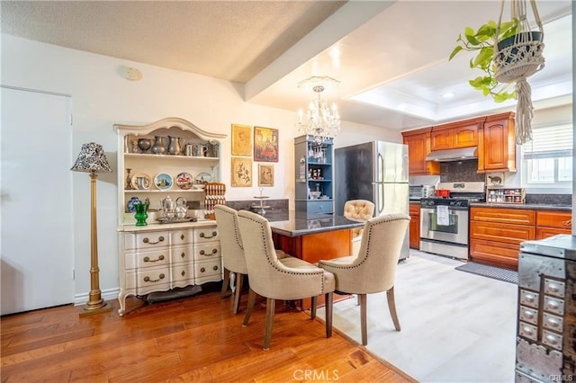 kitchen with a breakfast bar area, a chandelier, stainless steel appliances, light wood-type flooring, and under cabinet range hood