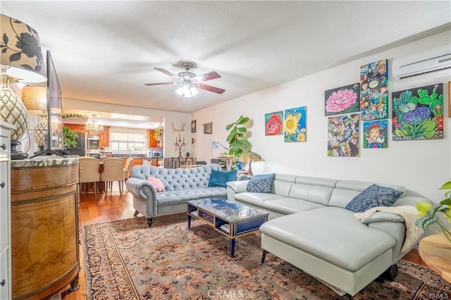 living area with an AC wall unit, wood finished floors, and ceiling fan with notable chandelier