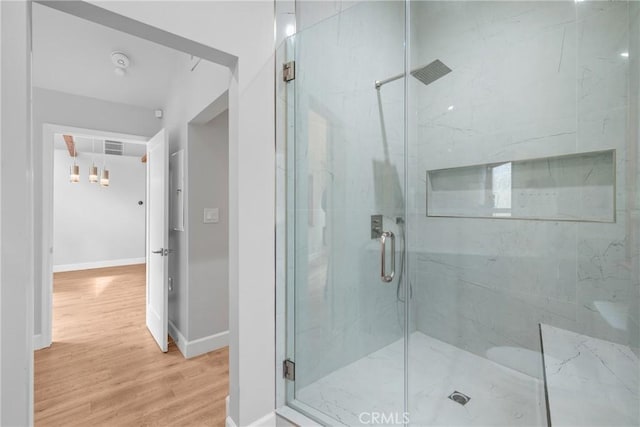 bathroom with a chandelier, a marble finish shower, baseboards, wood finished floors, and visible vents