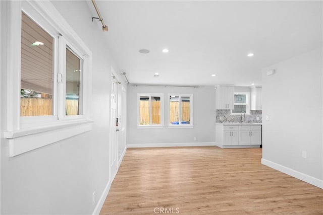 unfurnished living room with recessed lighting, baseboards, a sink, and light wood-type flooring