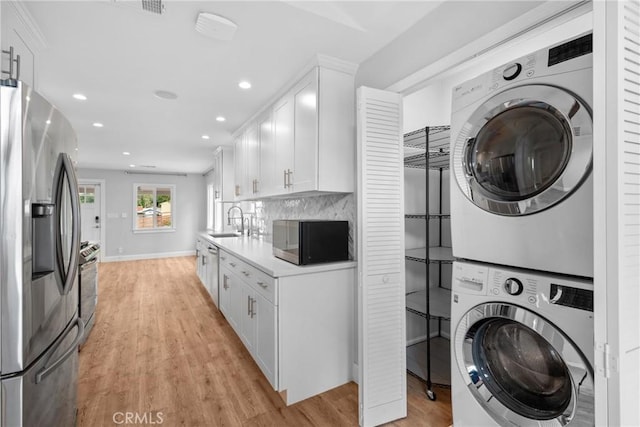 laundry area with laundry area, stacked washer and dryer, a sink, light wood finished floors, and recessed lighting