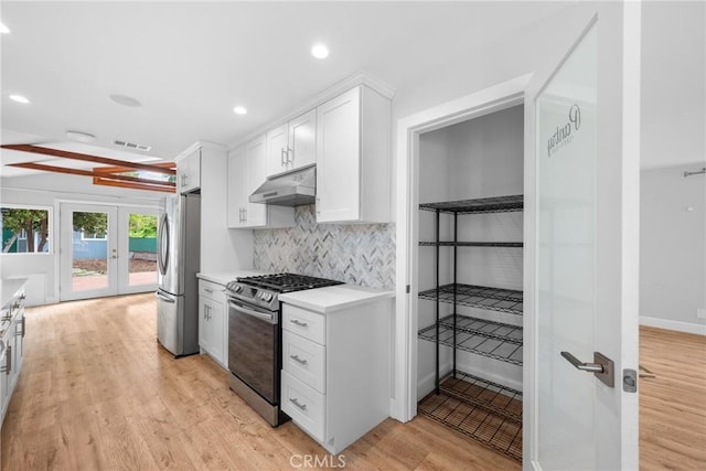 kitchen with white cabinets, appliances with stainless steel finishes, light wood-style flooring, decorative backsplash, and under cabinet range hood