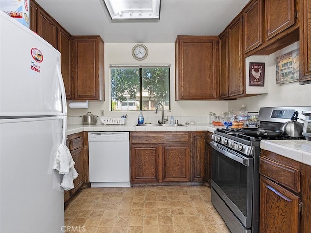 kitchen with a sink, tile counters, white appliances, and stone finish flooring