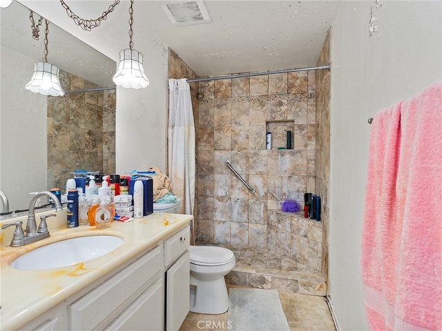 bathroom featuring vanity, toilet, tiled shower, and visible vents