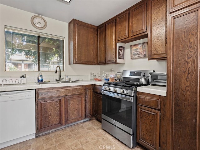 kitchen featuring stainless steel range with gas stovetop, a sink, dishwasher, and tile counters