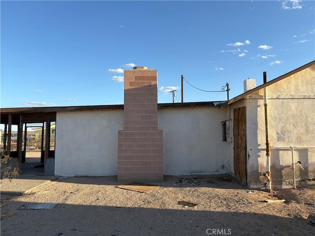 back of house featuring a chimney and stucco siding