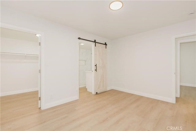 unfurnished bedroom featuring light wood-style floors, a barn door, baseboards, and a spacious closet