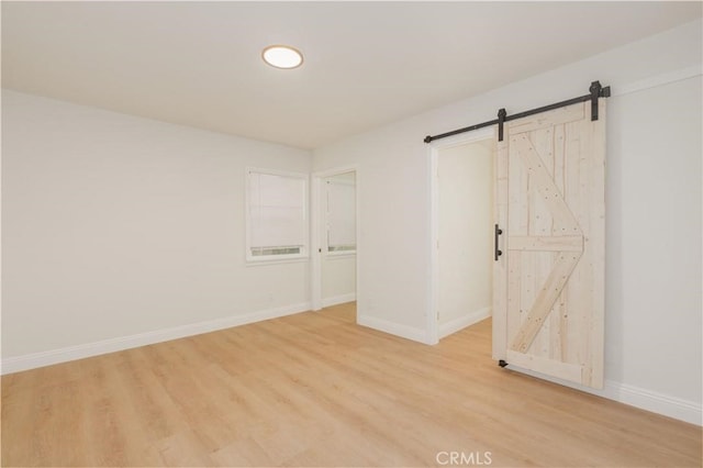 empty room with light wood-type flooring, a barn door, and baseboards