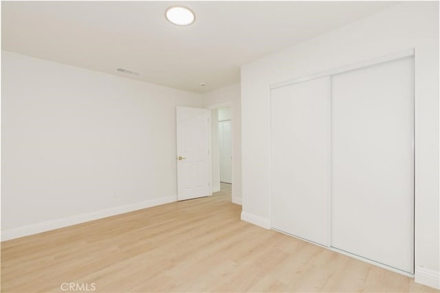 unfurnished bedroom featuring light wood-style floors, baseboards, a closet, and visible vents