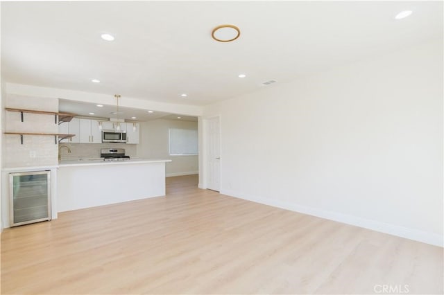 unfurnished living room featuring a sink, recessed lighting, baseboards, light wood-type flooring, and wine cooler