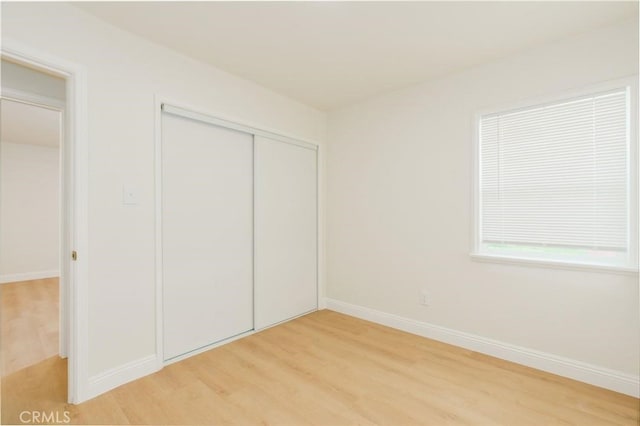 unfurnished bedroom with light wood-type flooring, baseboards, and a closet
