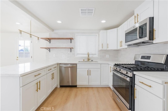 kitchen featuring visible vents, a peninsula, light wood-type flooring, a sink, and stainless steel appliances
