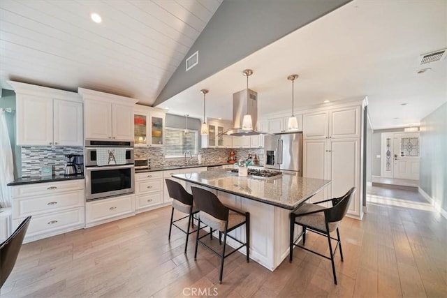9179 Hidden Farm Rd, Rancho Cucamonga, CA 91737 - kitchen featuring visible vents, island range hood, appliances with stainless steel finishes, lofted ceiling, and a breakfast bar